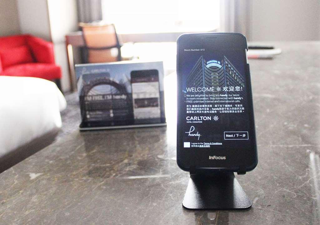 Carlton Hotel Singapore Camera foto The photo shows a smartphone set on a stand, displaying a welcome message in both English and Chinese. The phone appears to be part of a hotel service, likely providing information or functionality for guests. In the background, there is a small disp