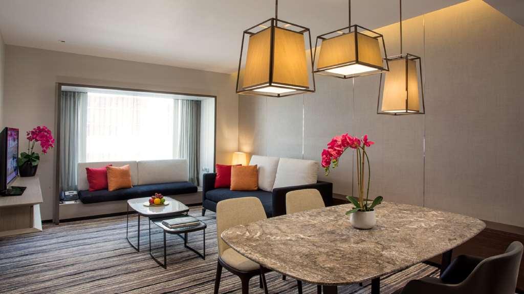 Carlton Hotel Singapore Camera foto The photo shows a modern living space that includes a cozy seating area and a dining area. 

1. **Seating Area**: On one side, there’s a sofa with decorative cushions in shades of red and orange, paired with a coffee table. A large window provides na