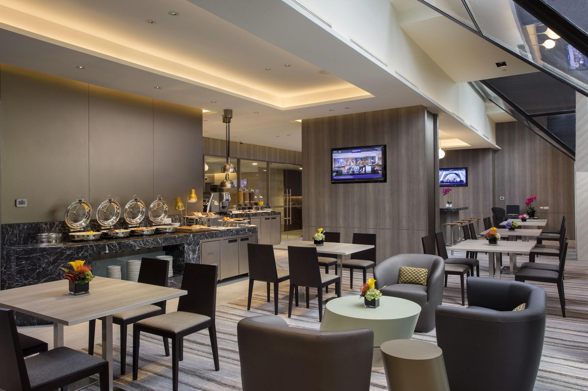 Carlton Hotel Singapore Esterno foto The photo depicts a modern dining area or café. It features a variety of tables and chairs arranged in a spacious setting. On one side, there is a buffet station with several stainless steel food containers. The walls are adorned with neutral-colored