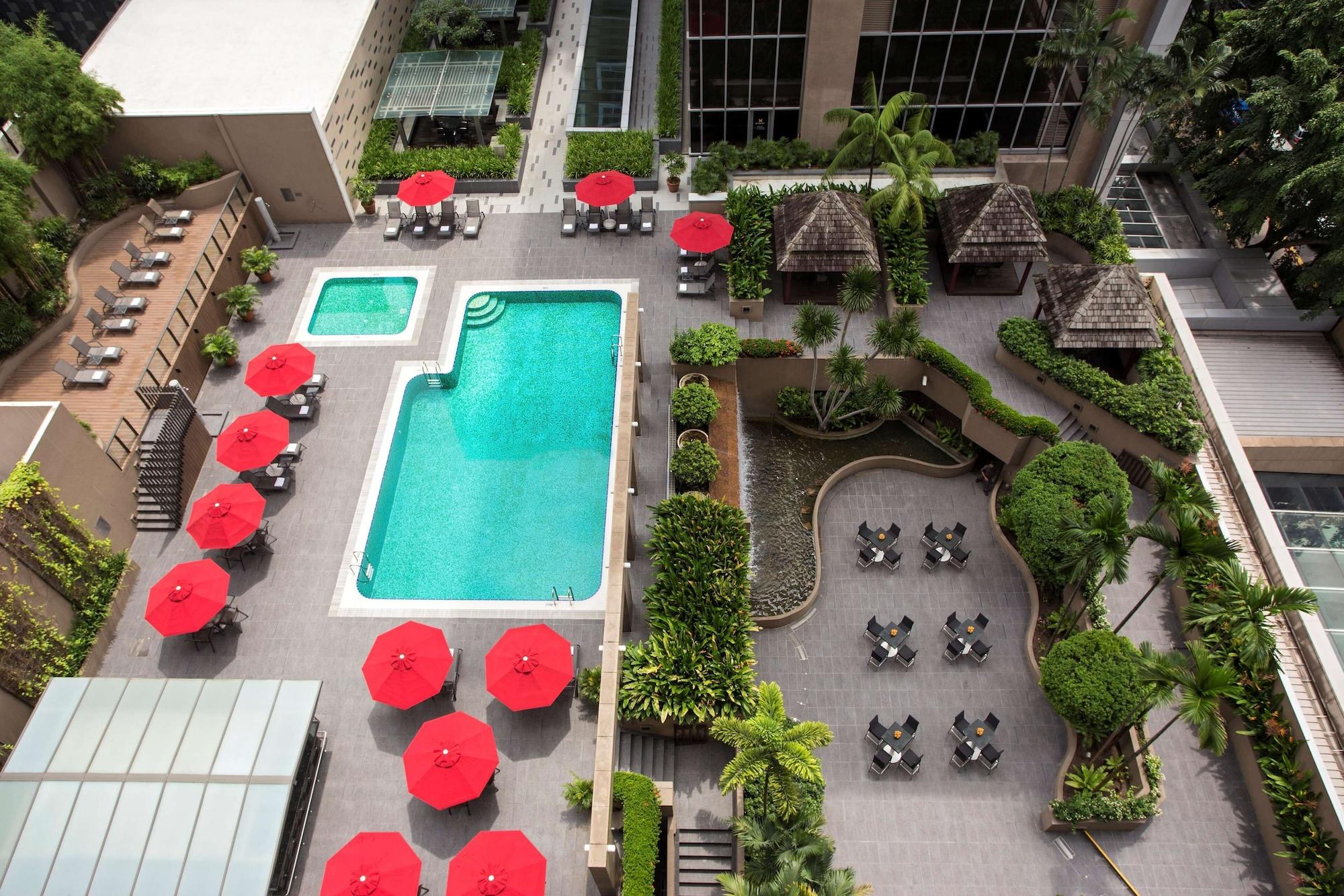 Carlton Hotel Singapore Esterno foto The photo shows a rooftop pool area with a large swimming pool featuring bright blue water. Surrounding the pool are several red umbrellas providing shade. There is also a smaller rectangular pool nearby. The area is landscaped with various greenery,