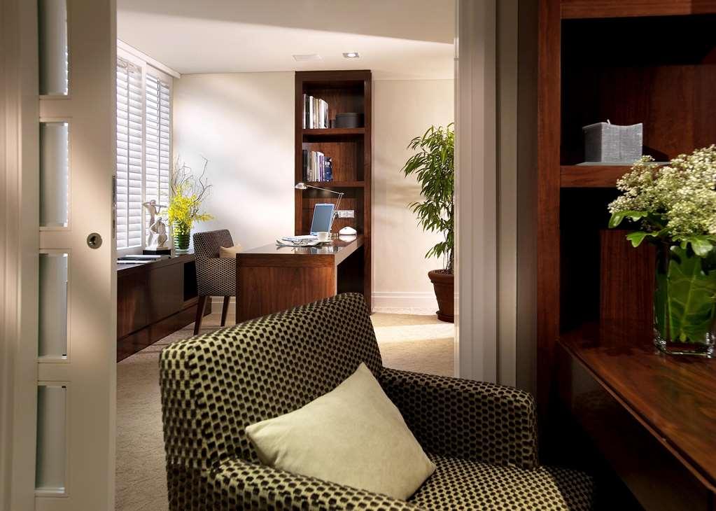Carlton Hotel Singapore Camera foto The photo depicts a contemporary office space. In the foreground, there is a patterned chair with a light-green cushion. The background shows an office area with a desk and a chair, positioned against a wall lined with bookshelves. There is a potted 