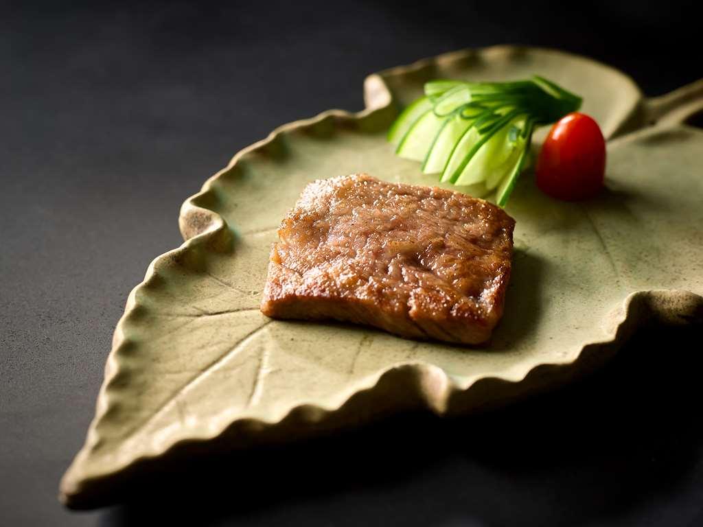 Carlton Hotel Singapore Ristorante foto The photo shows a piece of cooked meat, likely grilled or seared, presented on a green, leaf-shaped plate. Accompanying the meat are slices of cucumber and a small red tomato, arranged decoratively. The overall presentation emphasizes a simple yet el
