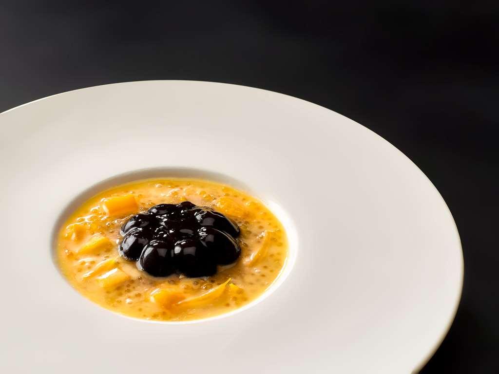 Carlton Hotel Singapore Ristorante foto The photo shows a dish presented on a white plate. At the center, there is a creamy base, likely a soup or purée, with a rich orange or yellow color. On top of this base is a mound of a dark, glossy substance, possibly a type of caviar or a similar i