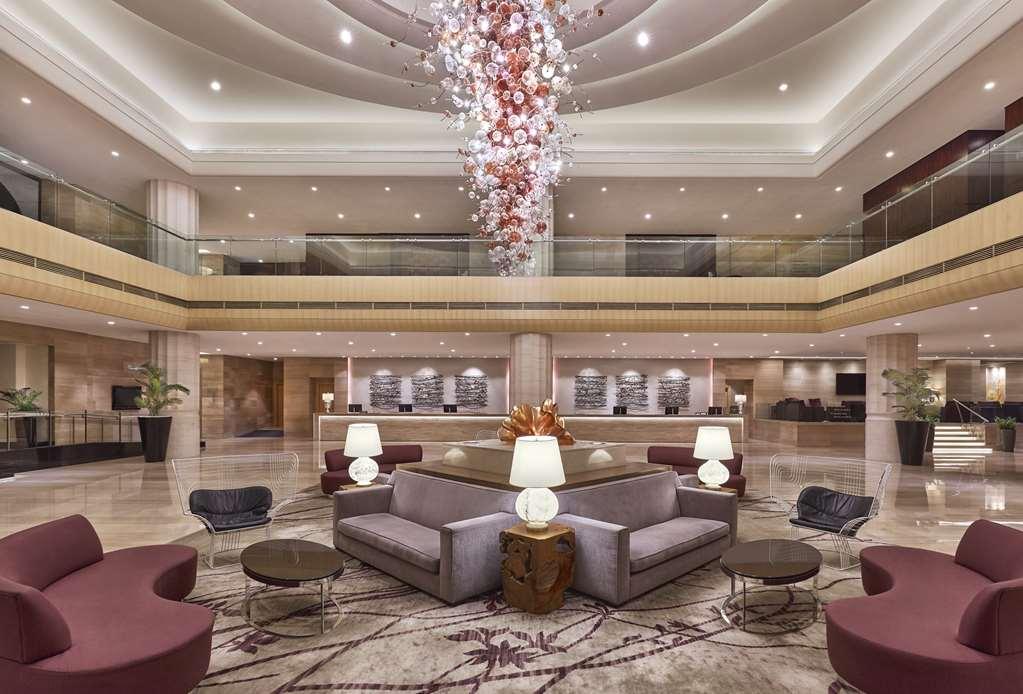 Carlton Hotel Singapore Interno foto The photo shows a spacious hotel lobby designed with a modern aesthetic. The area features a high ceiling and elegant lighting, highlighted by a striking chandelier made of intertwined shapes and colors. The seating arrangement includes comfortable s
