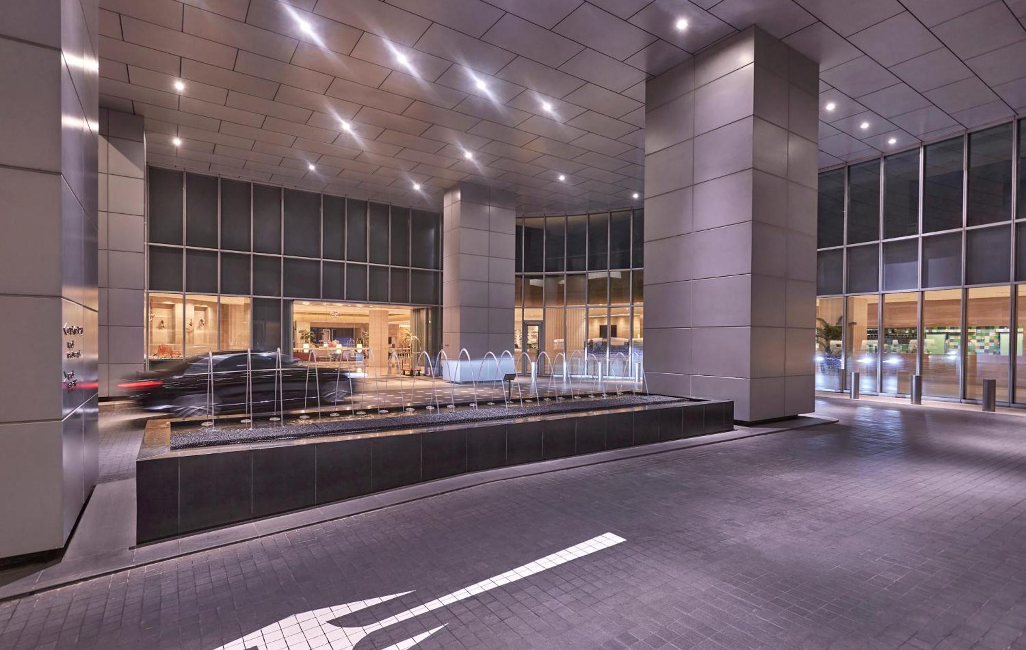 Carlton Hotel Singapore Esterno foto The photo shows the entrance of a modern building, likely a hotel or office complex. The area has large glass windows, allowing for natural light to enter. The architectural design features sleek, metallic columns and rhythmic lighting on the ceiling
