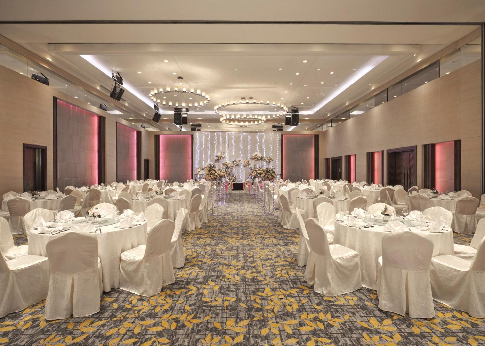 Carlton Hotel Singapore Esterno foto The photo shows a spacious banquet hall set for an event. The room features several round tables, each covered with white tablecloths, and neatly arranged with dinnerware. The chairs are also draped in white fabric. The floor has a patterned carpet w