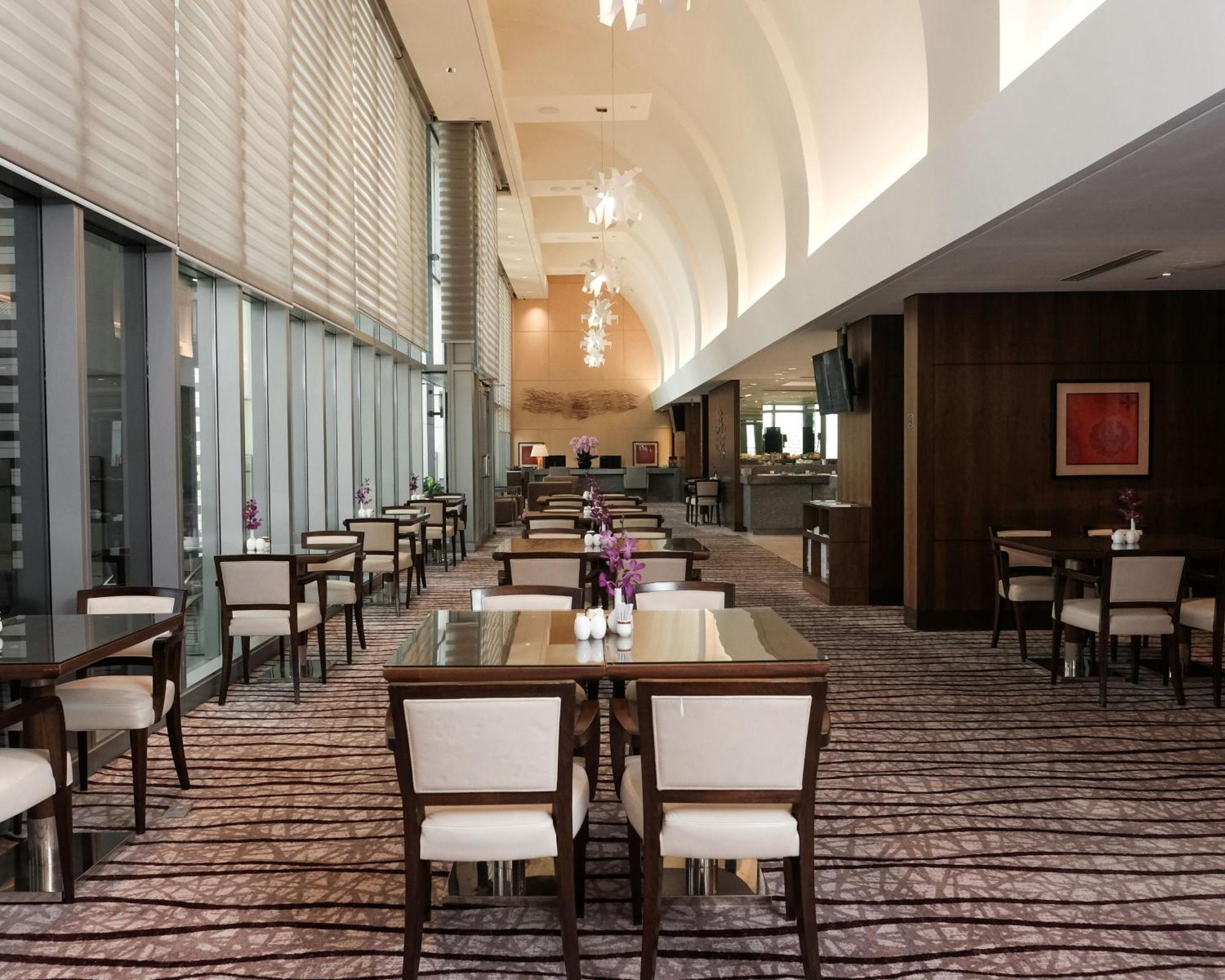 Carlton Hotel Singapore Esterno foto The photo shows the interior of a modern restaurant or dining area. It features a spacious layout with rows of wooden tables and upholstered chairs arranged neatly. The large windows allow natural light to fill the space, and there are elegant light 