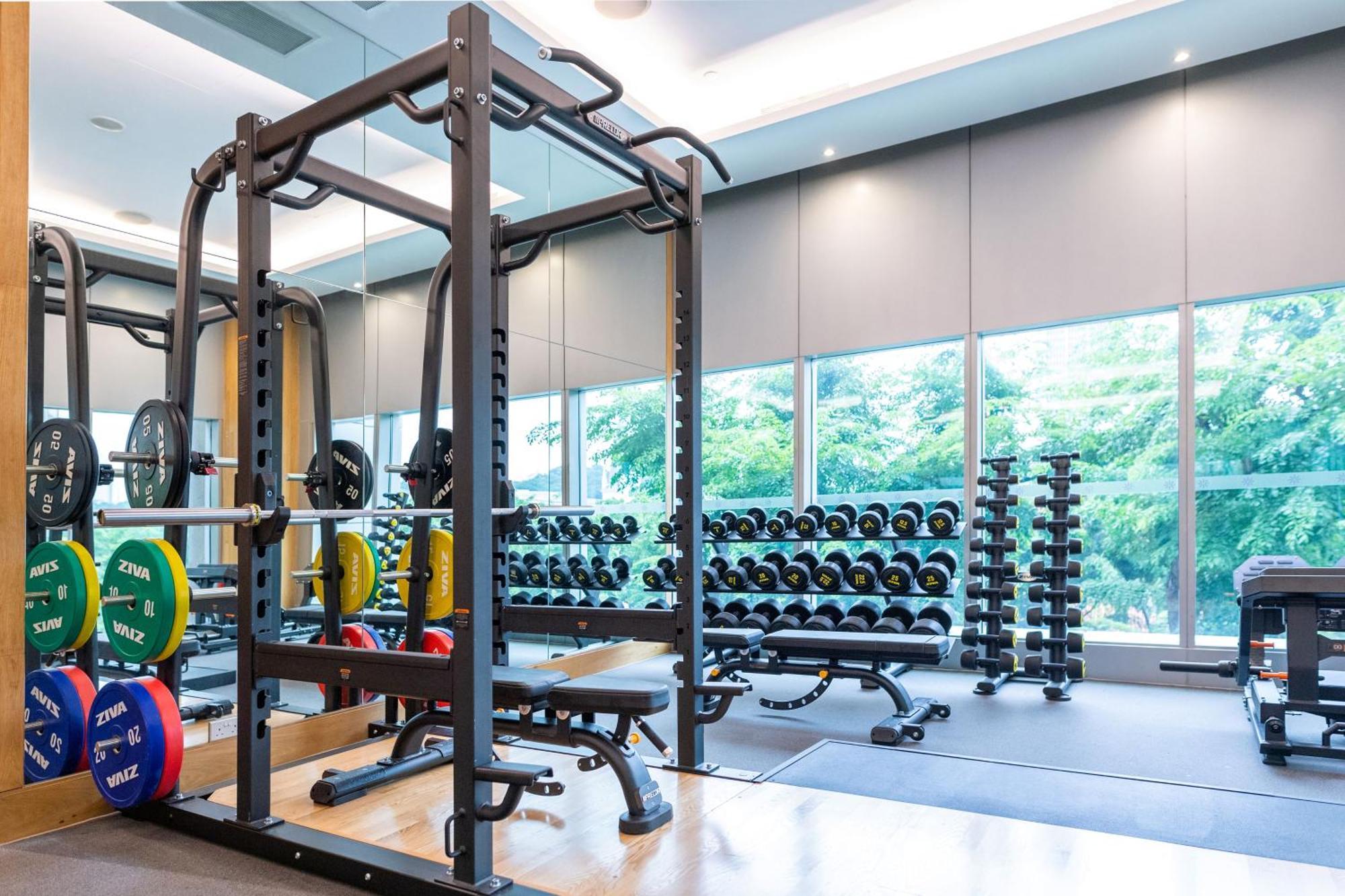 Carlton Hotel Singapore Esterno foto The photo shows a gym or fitness area. It features a weightlifting rack with various weights, a bench for exercises, and a squat rack. In the background, there are several rows of dumbbells on racks, indicating a well-equipped workout space. Large wi