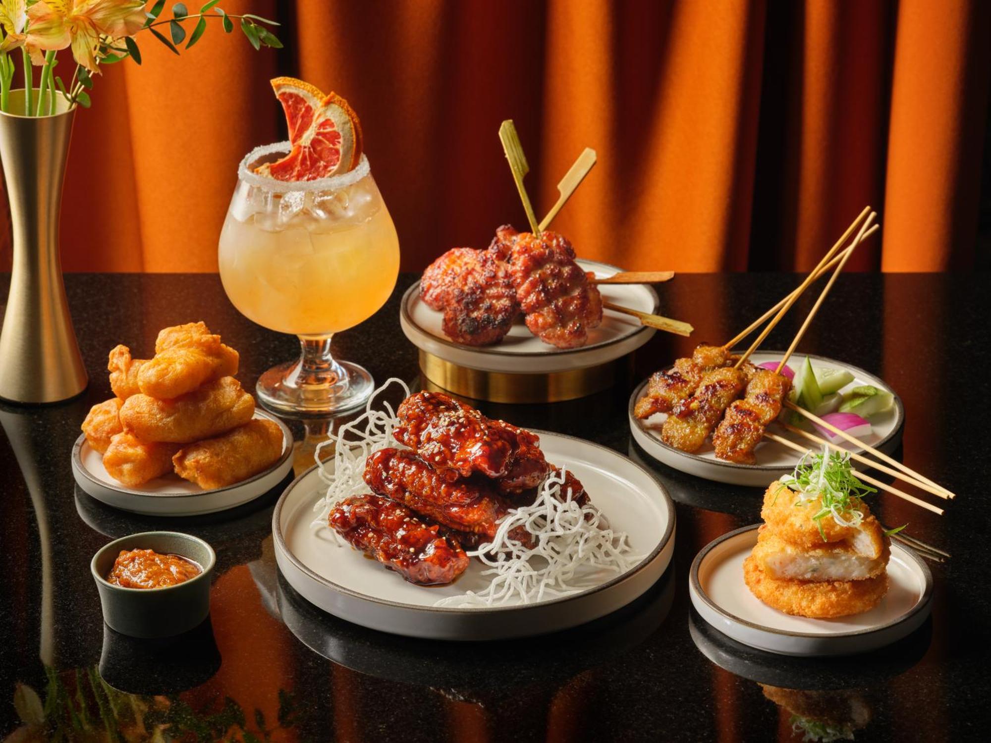 Carlton Hotel Singapore Esterno foto The photograph showcases an elegant spread of assorted dishes and a cocktail. 

1. **Main Dishes**: In the center, there is a plate with several fried chicken wings coated in a glossy red sauce, garnished with shredded lettuce or noodles.
2. **Appeti