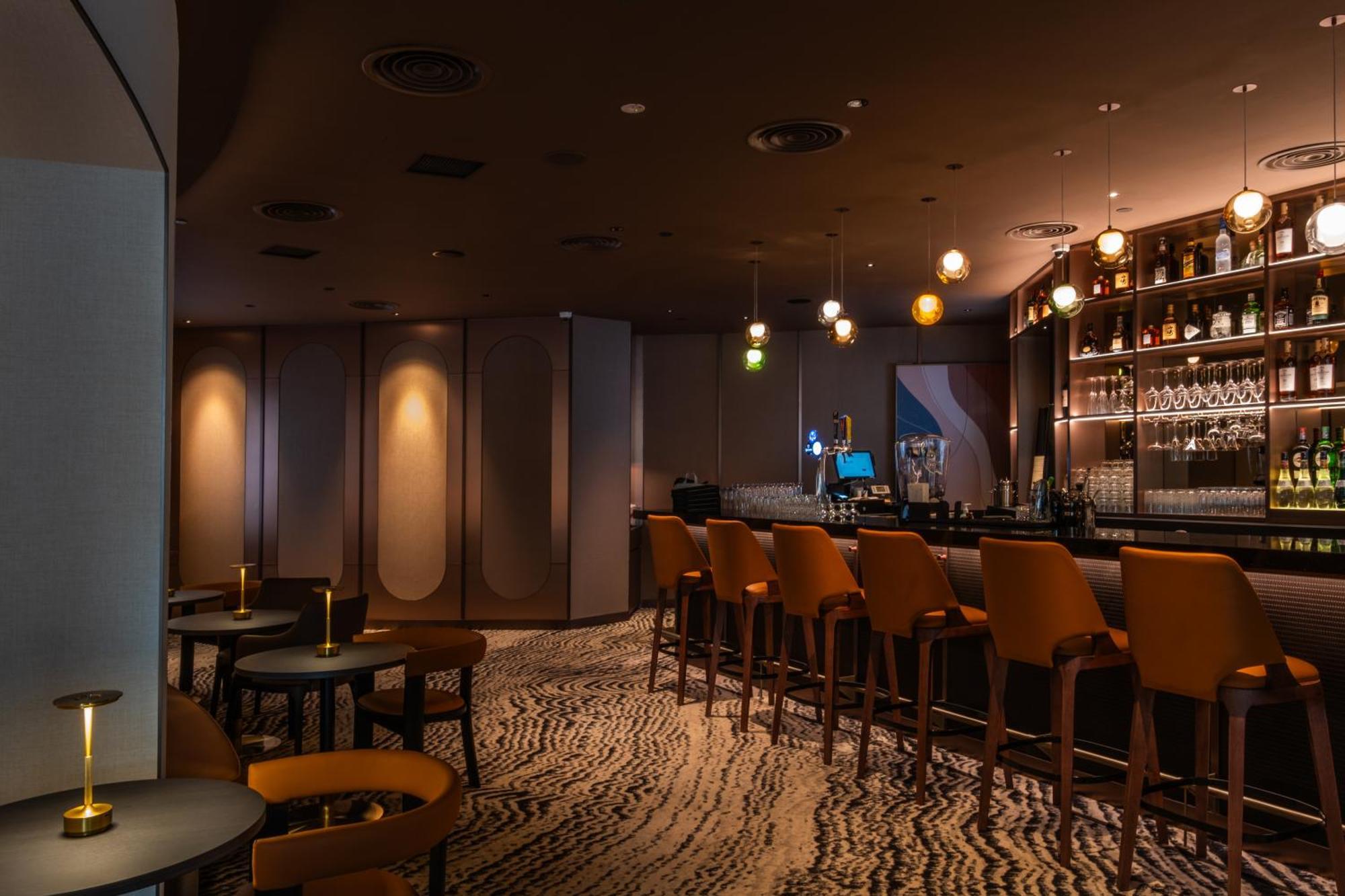Carlton Hotel Singapore Esterno foto The photo shows a modern bar interior. The space features a sleek bar counter with several high-backed chairs arranged in front. Behind the bar, there is a well-stocked shelf of various bottles. Soft lighting creates a warm and inviting atmosphere, w