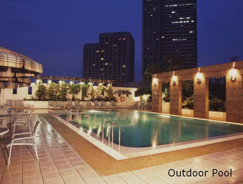 Carlton Hotel Singapore Servizi foto The photo shows an outdoor swimming pool area at night. The pool is illuminated, reflecting the surrounding lights. There are modern buildings in the background, and the area is decorated with potted plants and lighting fixtures along the poolside. A