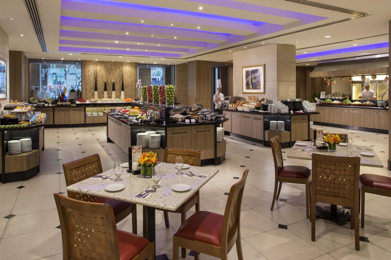Carlton Hotel Singapore Esterno foto The photo shows a restaurant dining area featuring a buffet setup. The space is well-lit, with modern decor and elegant furnishings. There are several food stations displaying a variety of dishes, likely including fruits, salads, and other culinary o